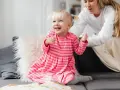 Uśmiechnięta dziewczynka w różowej sukience, która często mówi "kocham cię", bawi się z mamą na kanapie.